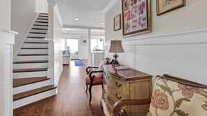 A staircase leading to a second floor, a wooden dresser, a chair, and a couch with a floral cushion. - C Street A - Incredible Ocean Front Condo in the heart of Wrightsville Beach (Wrightsville Beach)