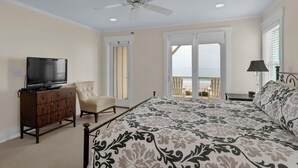 A bedroom with a bed, a television on a dresser, a chair, and a view of the beach through a sliding door. - C Street A - Incredible Ocean Front Condo in the heart of Wrightsville Beach (Wrightsville Beach)
