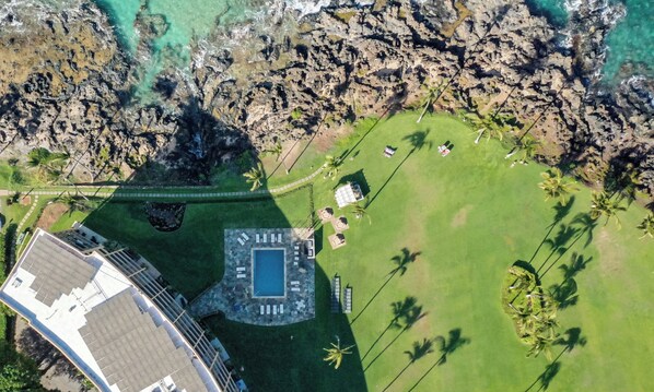 An aerial view of a resort with a swimming pool, lounge area, and palm trees.