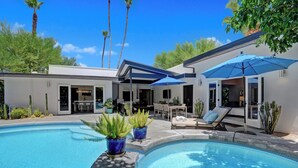 A modern outdoor pool area with a lounge chair and umbrella, surrounded by potted plants and a patio. - Palmera - Tahquitz River Estates Private Paradise! (Palm Springs)