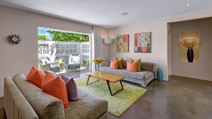 A modern living room with a sofa, a coffee table, and a couch with colorful cushions. There are abstract paintings on the walls and a vase with flowers on a side table. - Palmera - Tahquitz River Estates Private Paradise! (Palm Springs)