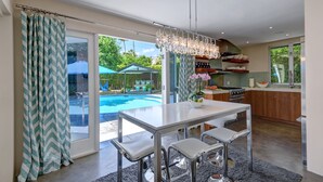 A modern kitchen with a dining area, large windows, and a view of a swimming pool. - Palmera - Tahquitz River Estates Private Paradise! (Palm Springs)