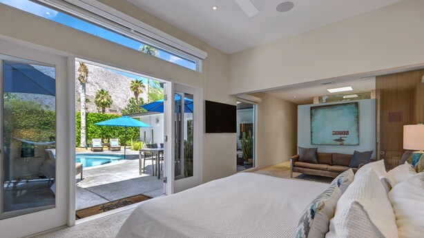 A bedroom with a large bed, a TV, and a view of a pool and outdoor seating area. - Palmera - Tahquitz River Estates Private Paradise! (Palm Springs)