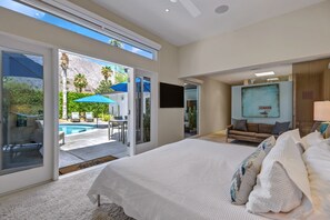 A bedroom with a large bed, a TV, and a view of a pool and outdoor seating area. - Palmera - Tahquitz River Estates Private Paradise! (Palm Springs)