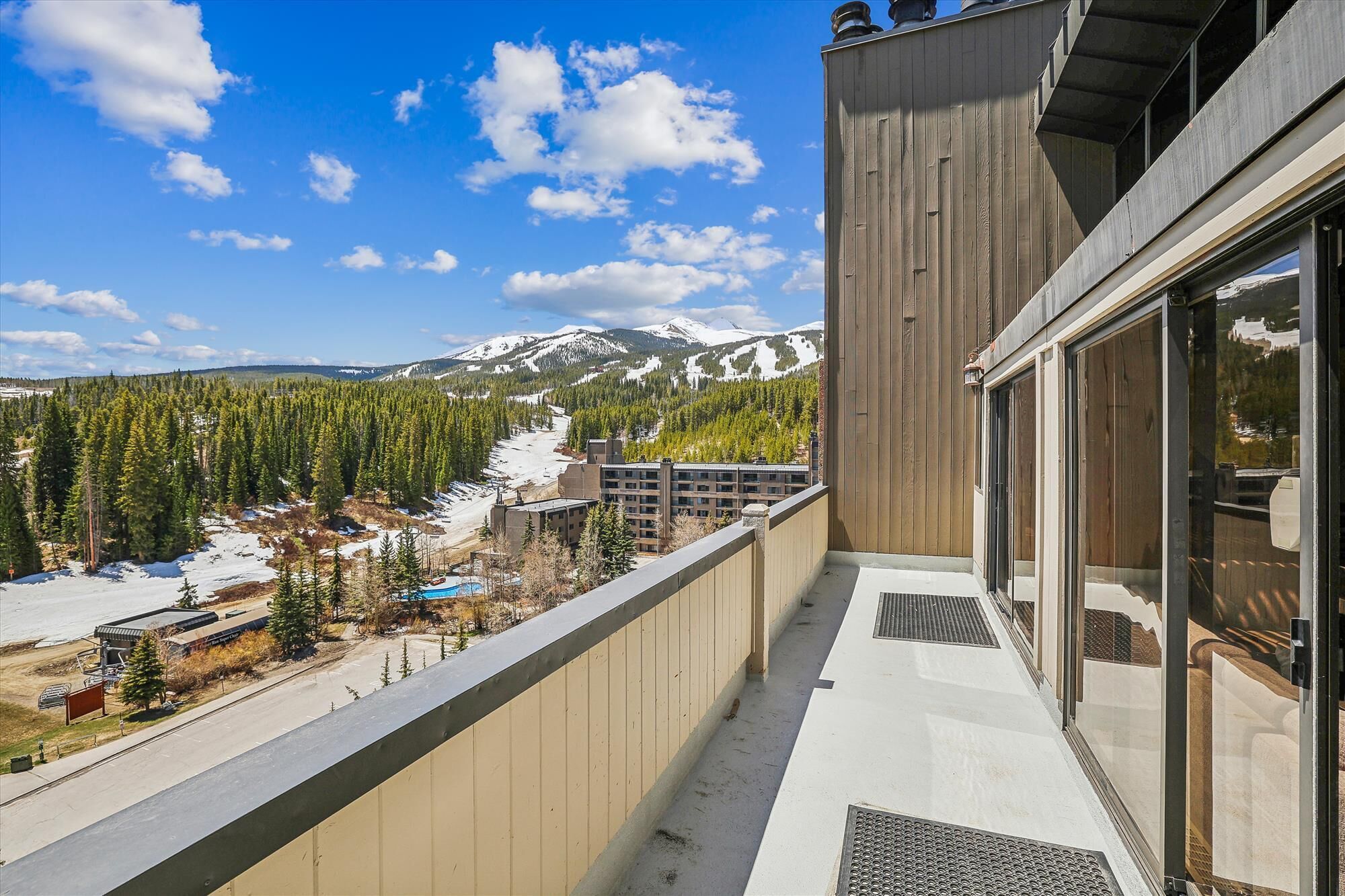 A balcony with a view of a snowy mountain range and a forested valley.
