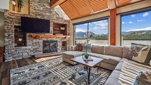 Un salon chaleureux avec une cheminée en pierre, un grand téléviseur à écran plat, un canapé et une vue sur les montagnes.