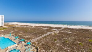 Blick auf einen Strand von einem Resort aus, mit Pool und Liegestühlen.