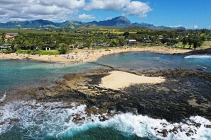 A coastal beach with clear waters, rocky areas, and a backdrop of mountains. - Kahala 614 Sunny Poipu  By Suite Paradise (Koloa)