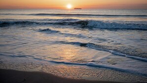 Ein Strand bei Sonnenuntergang mit Wellen und einem Schiff in der Ferne.
