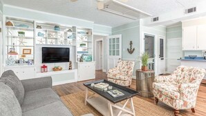 Un salon comprenant un téléviseur, deux fauteuils à motifs floraux, un canapé gris et une table basse.