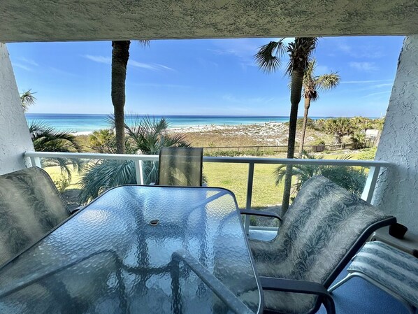 A balcony with a glass table and chairs, overlooking a beach and ocean.