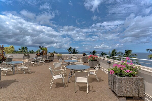 An outdoor patio with tables and chairs, overlooking a scenic ocean view.