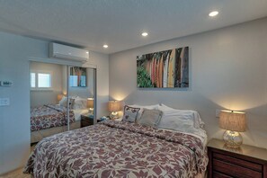 A bedroom with a large bed, a bedside table with a lamp, a mirror, and a wall-mounted artwork.