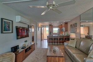 A modern living room with a flat-screen TV, a ceiling fan, a coffee table, and a leather sofa.