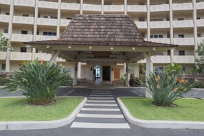 L’entrée d’un hôtel, avec un passage couvert, des palmiers et un bâtiment doté de balcons aux motifs décoratifs.