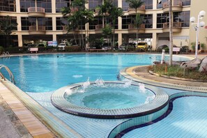 A large indoor swimming pool with a hot tub, surrounded by a multi-story building with balconies and palm trees. - Lagenda Condominium (Malacca City)
