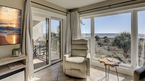 Un balcon spacieux offrant une vue sur la plage et l’océan, un fauteuil confortable et inclinable, ainsi qu’une petite table avec un magazine.