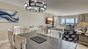 Un salon moderne comprenant un coin repas, un grand téléviseur et une vue sur l’océan.