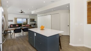 Una cocina moderna con una isla central, comedor con sillas y vista al océano.