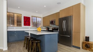Una cocina moderna con una isla central, armarios de madera, electrodomésticos de acero inoxidable y una pared decorada en azul.