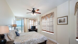 Une chambre avec un lit, un ventilateur de plafond, une télévision et un balcon avec vue.