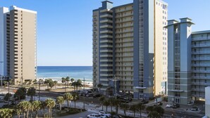 Un hôtel de grande hauteur doté de nombreux balcons, offrant une vue sur la plage et disposant d’un parking avec des voitures.