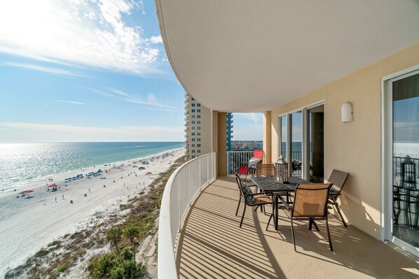 A balcony with a view of the beach and ocean, furnished with chairs and a table.
