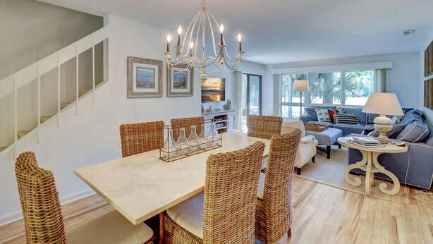 A spacious living area with a dining table, wicker chairs, a chandelier, and a sofa with a view of the outdoors.