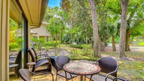 An outdoor patio with wicker furniture and a tiled table, surrounded by trees and greenery.
