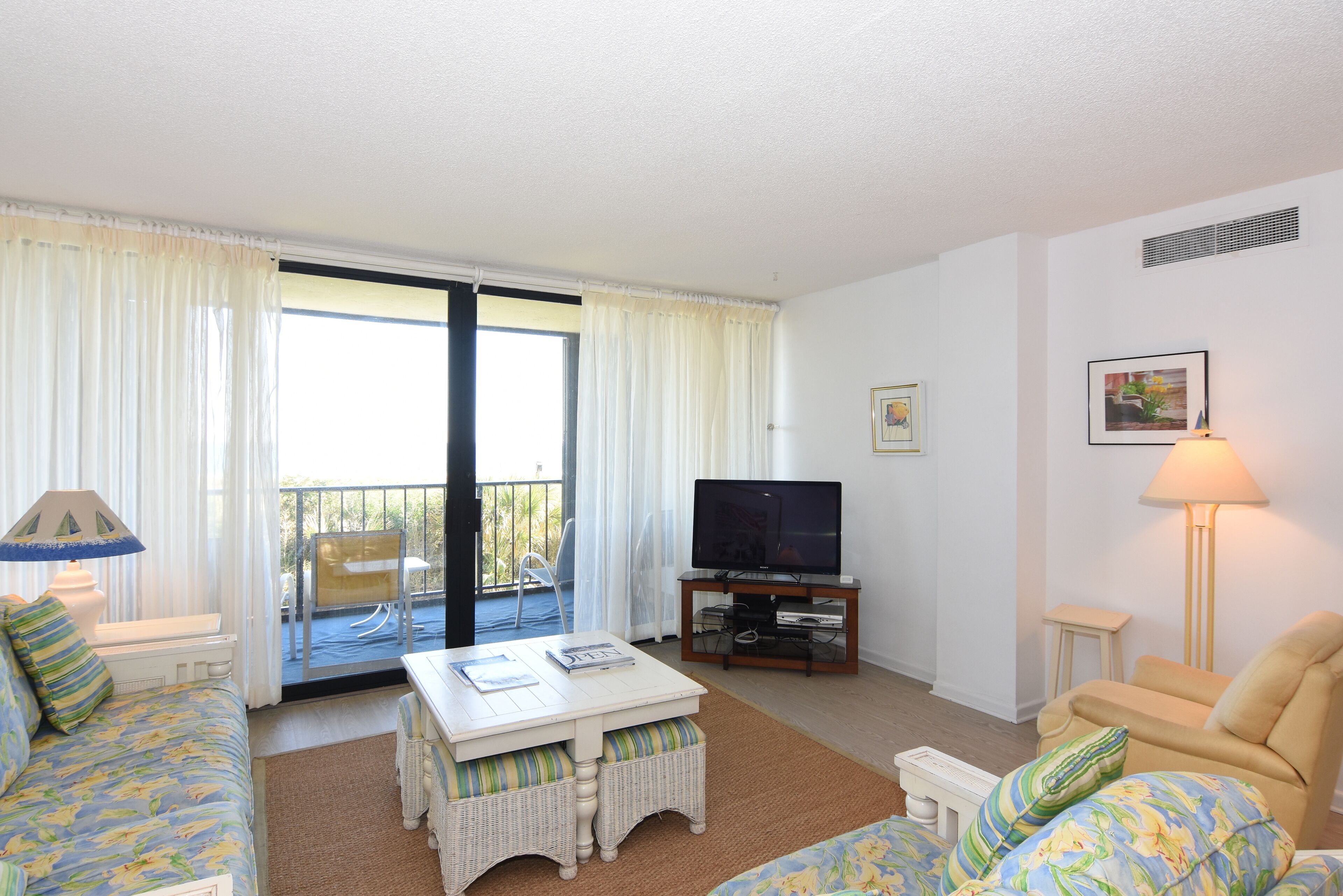 Ein Wohnzimmer mit einer Couch, einem Couchtisch, einem Fernseher und einem Balkon mit einem Stuhl.