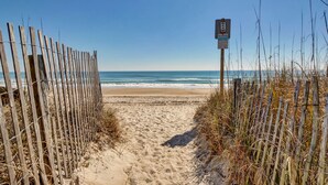 A sandy beach path leading to the ocean, flanked by wooden fences and a signpost.