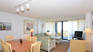 A living room with a sofa, a TV, a dining table with chairs, and a balcony with curtains.