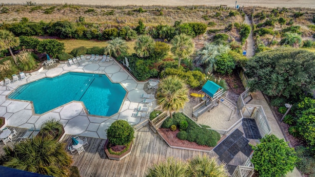 An aerial view of a resort with a swimming pool, deck chairs, and a beach view.