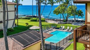 A pool area with a view of the ocean, surrounded by palm trees and lounge chairs. - 🏖️Top Floor Kona Condo w/ Ocean Views + Full A/C (Kailua Kona)