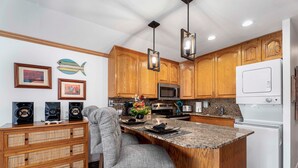 A kitchen with wooden cabinets, a granite countertop island, a built-in microwave, and a white refrigerator. - 🏖️Top Floor Kona Condo w/ Ocean Views + Full A/C (Kailua Kona)