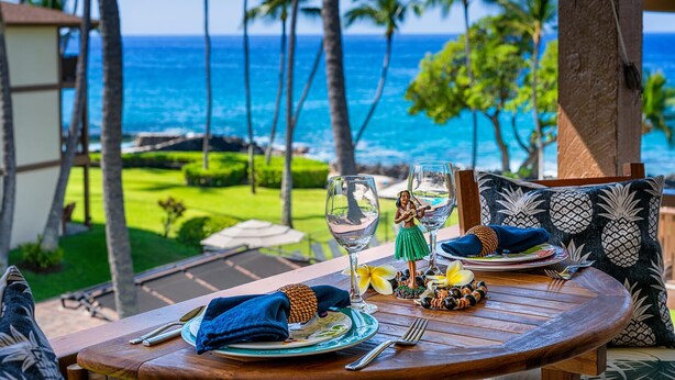 A table set for two with a view of the ocean and palm trees. - 🏖️Top Floor Kona Condo w/ Ocean Views + Full A/C (Kailua Kona)