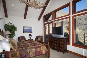 A bedroom with a large bed, a dresser, a television, and a window with a mountain view.
