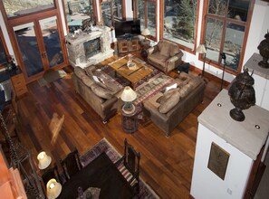 Relax in this spacious living area with a high ceiling and large windows offering a view of the outdoors. Features a stone fireplace, comfortable sofa, and a television.