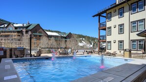 A pool area with a sign indicating a 3ft depth, surrounded by buildings and a snowy mountain backdrop.
