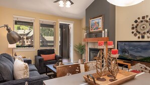 A cozy living room with a fireplace, a television, and a large window overlooking a scenic view.