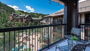 A balcony with outdoor seating, overlooking a pool and a mountainous landscape.