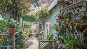A garden with a wooden table and chairs, surrounded by various plants and a bamboo fence. - Adorable Cozy Studio (Stinson Beach)