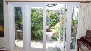 A room with a piano, a door leading to a garden, and a view of the garden through the door. - Adorable Cozy Studio (Stinson Beach)