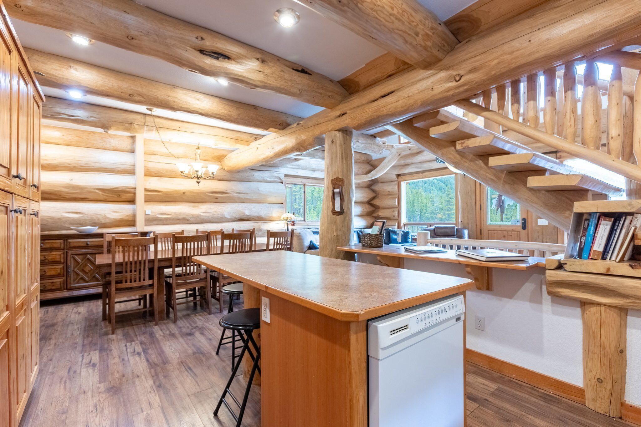 Ein Holzblockhaus-Interieur mit Küchenbereich, der Holzbalken, eine zentrale Kochinsel und einen Geschirrspüler zeigt.
