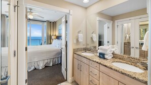 A hotel room with a bed, a bathroom with a large mirror, a sink, and a view of the ocean. - Island Tower 1001 by Liquid Life (Gulf Shores)