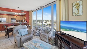 A spacious living area with a large TV, comfortable seating, a kitchen, and a view of the beach. - Island Tower 1001 by Liquid Life (Gulf Shores)