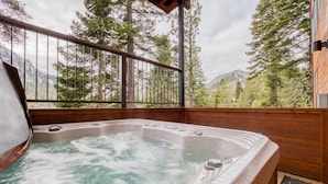 Ein Whirlpool mit Holzterrasse und Blick auf einen bewaldeten Gebirgszug.