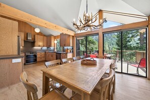 A modern kitchen with wooden cabinets, a large dining table, and a view of the outdoors. - Juniper at Alpine - Private Hot tub, Pet Friendly & Amazing Views! (Alpine Meadows)