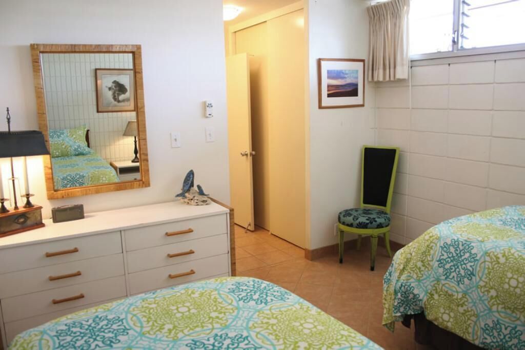 A bedroom with two beds, a dresser, a chair, a mirror, and a door leading to another room.