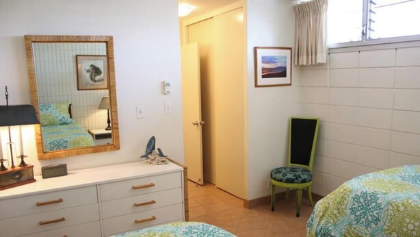 A bedroom with two beds, a dresser, a chair, a mirror, and a door leading to another room.